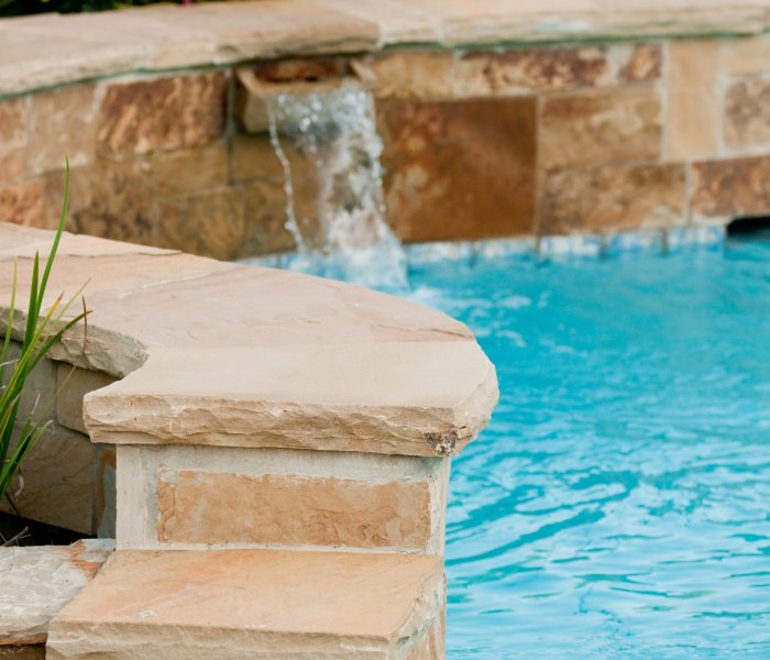 Beautiful swimming pool with flagstone wall that has waterfall pouring out of it.